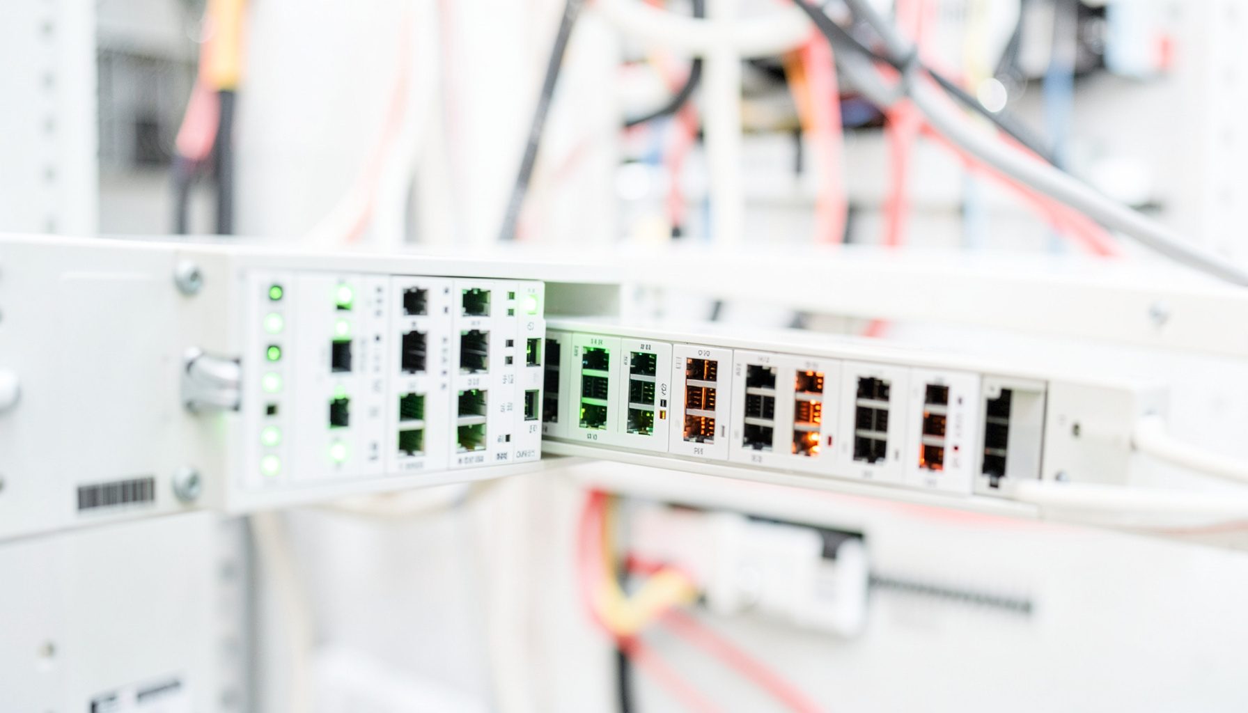 A bright, airy close-up of a rack-mounted network switch with glowing green and amber port LEDs, set against a softly lit server-room backdrop with clean cable management