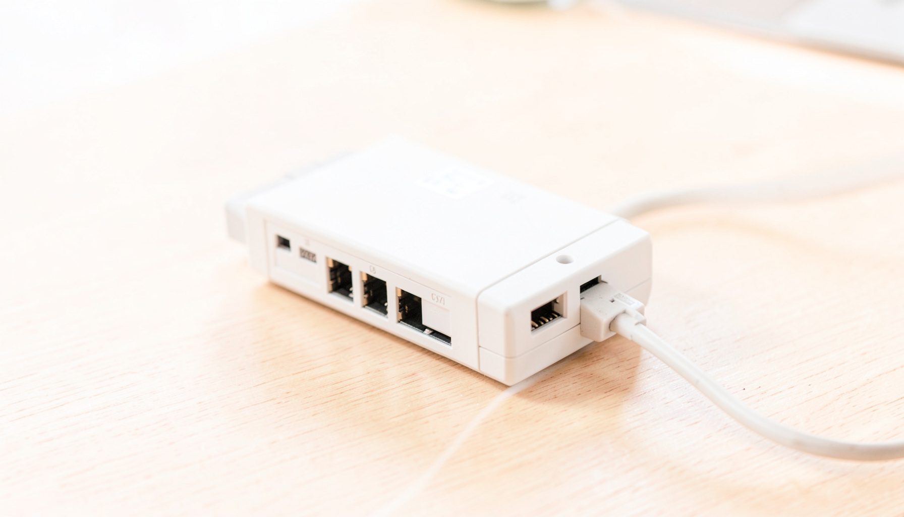 Ethernet surge protector device with multiple RJ45 ports and grounding wire, photographed on a light wooden desk surface