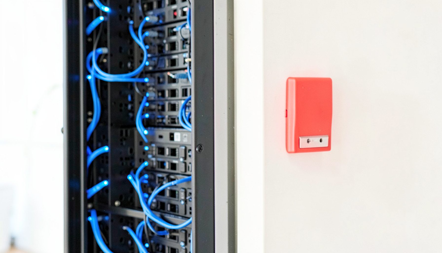 Dark server rack with glowing blue network cables and a prominent red security lock switch on a wall panel